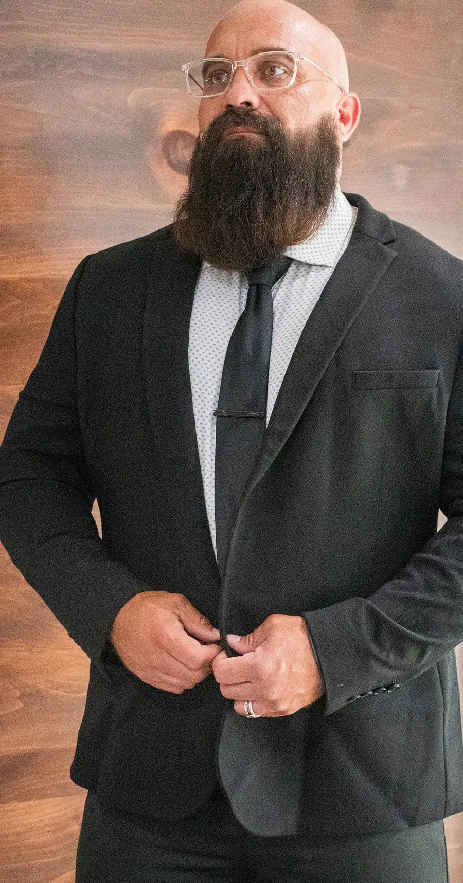 Shannon Cain buttoning a dark suit jacket in front of a wood wall